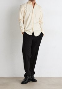 Camicia gialla chiara con bottoni abbinata a pantaloni neri e scarpe. La camicia presenta un collo e una vestibilità comoda, mentre i pantaloni sono a gamba larga.