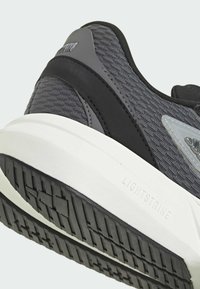 Szare buty sportowe z teksturowaną cholewką, eleganckimi czarnymi akcentami i białą podeszwą środkową z brandingiem "LIGHTSTRIKE" po boku.