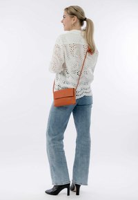 Weiße Bluse mit Augenlochmuster und gemusterten Ausschnitten, kombiniert mit hellblauen Jeans und schwarzen Stiefeletten. Braune Umhängetasche mit Klappenverschluss.