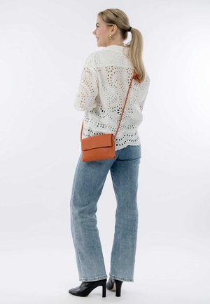 Weiße Bluse mit Augenlochmuster und gemusterten Ausschnitten, kombiniert mit hellblauen Jeans und schwarzen Stiefeletten. Braune Umhängetasche mit Klappenverschluss.