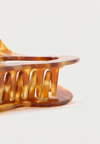 Um clip de cabelo em tortoiseshell castanho, feito de plástico brilhante, com uma silhueta ondulada, dentes verticais e uma base arredondada para melhor aderência.