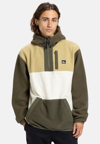 Fleece mikina s kapucí v zeleno-bežovo-bílé barevné blokové kombinaci, s kapsou na zip vpředu a nastavitelnou kapucí se stahovacími šňůrkami.