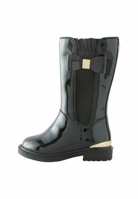 Stivale alla caviglia in patent nero con finitura lucida, pannello laterale elastico, dettaglio a fiocco e tacco metallico dorato. Suola robusta con grip texturizzato.