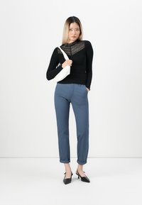 Svart långärmad topp med strukturerad spetsdesign, i kombination med blå byxor med uppvikt fåll och svarta spetsskor. Vit axelremsväska.