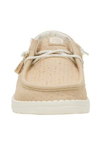 Scarpa di tela beige con una finitura testurizzata, suola in gomma bianca, marchio ben visibile sulla linguetta e lacci decorativi con pon-pon.