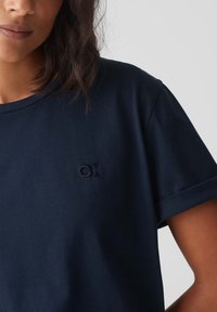 T-shirt in cotone blu navy con maniche corte, caratterizzato da un piccolo logo ricamato sul petto e polsini delle maniche arrotolati. Texture liscia.