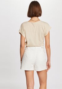 Top de manga corta en beige claro con mangas remangadas, combinado con pantalones cortos blancos de talle alto con bolsillos traseros y detalles de costura sutiles.