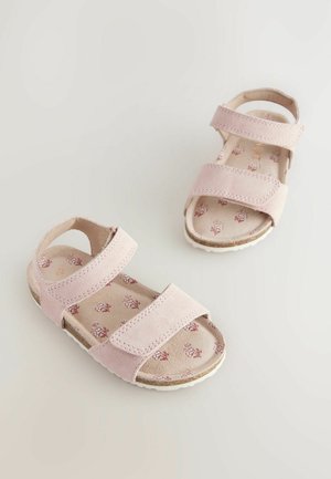 Sandale roz din suede cu două curele reglabile, spate deschis și branț cu model floral. Talpă din cauciuc alb cu profil pentru aderență.