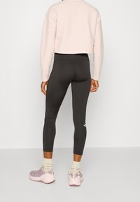 Przycięty jasnoróżowy sweter, czarne legginsy i szare sneakersy z różowymi akcentami. Zauważalne szczegóły: ściągacze i teksturowane skarpetki.