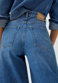 Hoch geschnittene blaue Jeans aus Denim in lässiger Passform, mit zwei Gesäßtaschen und einem gebrandeten Lederpatch am Bund.