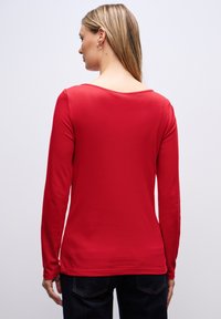 Rode long sleeve top met een ronde hals, zachte textuur, aansluitend ontwerp en naadloze schouders. Gecombineerd met donkere jeans.