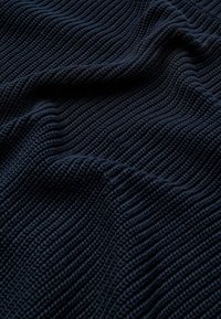 Tissu texturé bleu foncé avec un motif côtelé ondulé. Le matériau semble doux et tissé, mettant en valeur la profondeur avec une variation de lumière et d'ombre.