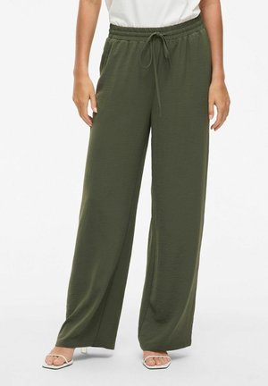Pantaloni a gamba larga verde oliva realizzati in un tessuto testurizzato, con una vita elastica dotata di cordoncino. Abbinati a sandali con le dita scoperte.