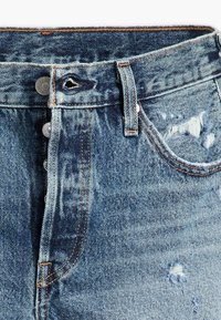 Jeans de mezclilla azul claro de cintura alta, con cierre de botón, acentos deshilachados y detalles sutilmente desgastados.