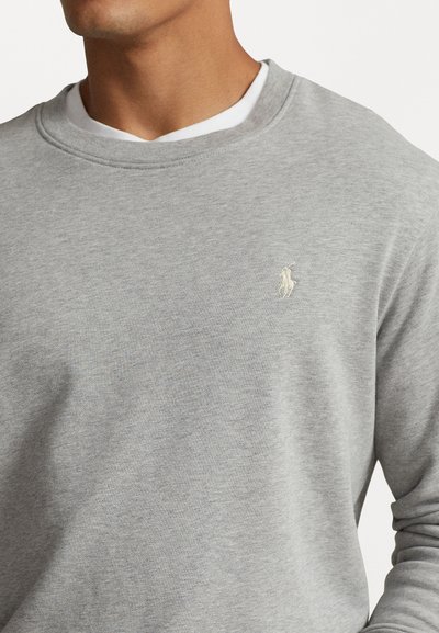 Sivi dukserica s okruglim izrezom, izrađena od mješavine pamučnih tkanina. Ima mali, izvezeni logo u kontrastnoj boji na prsima.