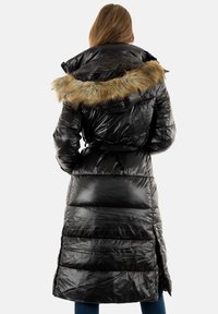 Abrigo largo negro acolchado con una textura brillante, un borde de pelaje sintético en la capucha y una cintura ceñida con cinturón. Presenta un diseño de costura vertical.