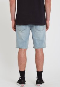 Light blue denim shorts with rolled hems, featuring two back pockets, worn with black crew socks and black sneakers.