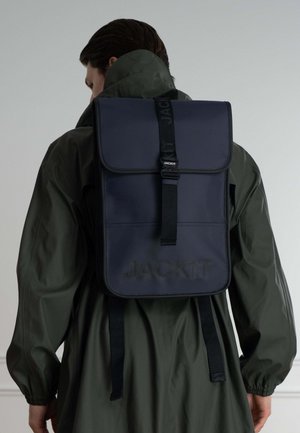 Zaino navy realizzato in materiale liscio, con chiusura a pattina, spallacci neri regolabili e marchio in rilievo sulla parte anteriore.