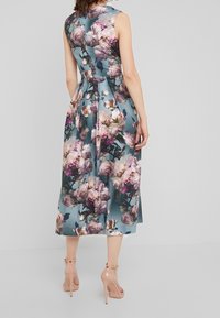 Blommig midi-klänning i blått tyg, med midjefuzz, ärmlös design och stora rosa och vita blommor. Kombineras med nude-hälar.