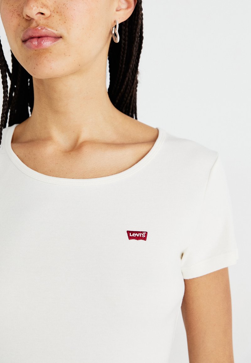 T-shirt en coton blanc avec un col rond et des manches courtes. Présente un petit logo rouge Levi's sur le côté gauche. Texture lisse.