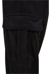 Poche de pantalon cargo en tissu côtelé noir avec rabat, mettant en valeur les détails de texture et de couture.