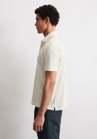 Short-sleeve polo shirt in off-white, featuring a two-button collar, side slits, and a soft textured fabric.