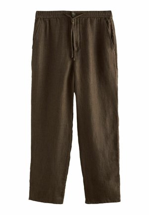 Nahaufnahme von dunkelbraunen, texturierten Stoffhosen mit einer quadratischen Gesäßtasche und sichtbaren Nähten an der Hüfte und Hand einer Person.