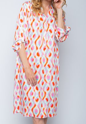 Femme portant une robe mi-longue à manches longues avec un motif géométrique multicolore en tons de rose, orange et turquoise.