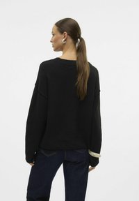 Musthave mustamustärviga oversize-sviiter, tekstureeritud viimistlusega, ümmargune kaelus, langenud õlad ja pikad varrukad; sobitatud tumedate siniste teksadega.