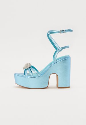 Sandali platform metallici blu con tacco spesso, caratterizzati da cinturini incrociati e un accento di gioiello nella zona delle dita.