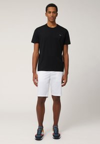 Zwarte katoenen T-shirt met korte mouwen en een ronde hals, gecombineerd met witte shorts. Model draagt kleurrijke sportschoenen.