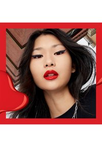 Porträtt av en person med mörkt hår, som bär röd läppstift och djärv svart eyeliner, inramad av en livlig röd bakgrund och glänsande accenter.