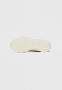 Suola di una sneaker beige con un motivo a nido d'ape, mostrata su uno sfondo bianco puro.