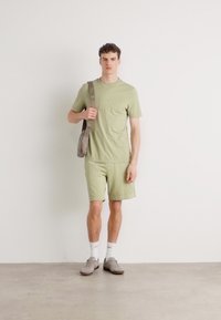Light green cotton t-shirt and shorts set, featuring embossed logo, paired with grey shoes and a beige crossbody bag. Simple, casual design.