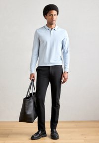 Polo bleu clair à manches longues, pantalon noir ajusté, mocassins noirs et un grand sac fourre-tout noir. Tissu lisse et design épuré.