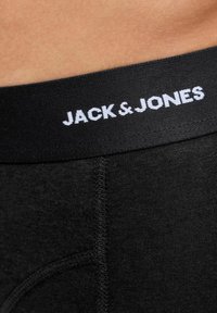 Black underwear with a wide waistband featuring white text that reads "JACK & JONES." Smooth texture with a fitted design and visible stitching.