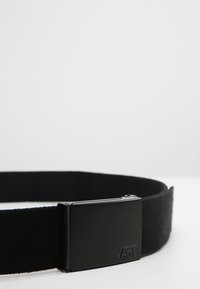 Black fabric belt featuring a matte black metal buckle with "VANS" engraved. The belt is flat and smooth, with a simple design.