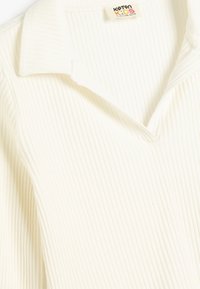 Gestreiftes Poloshirt aus weichem, cremefarbenem Stoff mit klassischem Kragen. Ein Etikett ist am Halsansatz angebracht.
