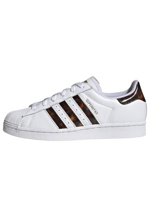 Biały sneaker Adidas Superstar z brązowymi paskami w kolorze muszli żółwia i patką na pięcie, gumowym noskiem w skorupie oraz sznurowaniem, widok z boku.