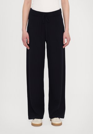 Black wide-leg pants with a drawstring waistband, made of soft fabric, feature a smooth texture and cuffed hems, paired with light shoes.