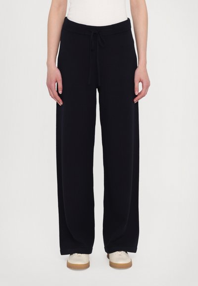 Zwarte wijde broek met een verstelbare tailleband, gemaakt van zachte stof, heeft een gladde textuur en omslagranden, gecombineerd met lichte schoenen.