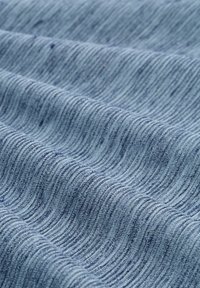 Jasnoniebieska tkanina o subtelnej strukturze prążkowanej, ukazana w miękkich fałdach, podkreślająca swoje wzory tkane i delikatne różnice kolorystyczne.