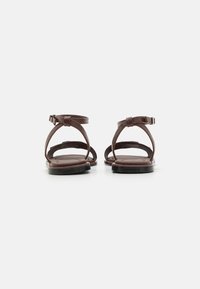 Sandales en cuir marron avec de fines brides à la cheville et une semelle plate. Présente un design épuré et un style minimaliste, vue de l'arrière.
