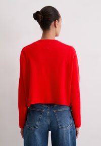 Pull court rouge en tricot doux, doté de longues manches et d'un col rond, associé à un jean bleu taille haute.