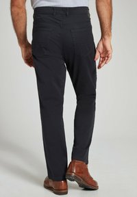 Donkerblauwe slim fit broek, met twee achterzakken en een soepel textuur, gecombineerd met bruine leren enkelboots.