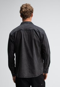 Zwarte denim shirt met een button-down kraag, lange mouwen met een knoopsluiting bij de manchetten, en een gestructureerde stof met contrasterende stikdetails.
