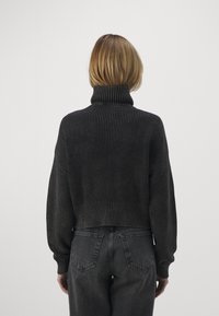 Gekürzter, dunkelgrauer Strickpullover mit hohem Kragen, geripptem Muster und weiten Ärmeln, kombiniert mit hochtaillierten, dunkelblauen Jeans.