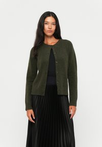 Dark green cardigan made of soft material, featuring a round neckline, button closures, and a relaxed fit, worn over a black pleated skirt.
