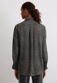 Long-sleeve, collared shirt in black with white floral pattern. Soft fabric, slightly loose fit, buttoned cuffs, and back yoke detail.