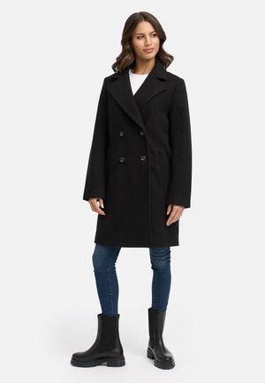 Schwarzer doppelt knöpfbarer Mantel mit großen Revers, seitlichen Taschen und sechs Knöpfen. Kombiniert mit blauen Jeans und schwarzen Stiefeletten. Glatte Textur.